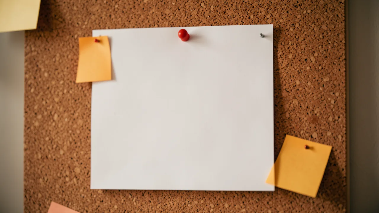 Calendario de papel en blanco clavado en un tablero de corcho con notas adhesivas de color ámbar